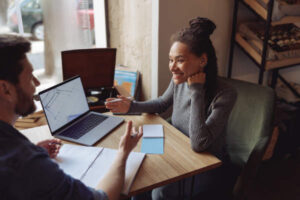 Cheerful Young Stylish Woman At Meeting With Male Partner In Cafe. Discussing Startup At Laptop. - ContSmart Contabilidade e Corretora de Seguros